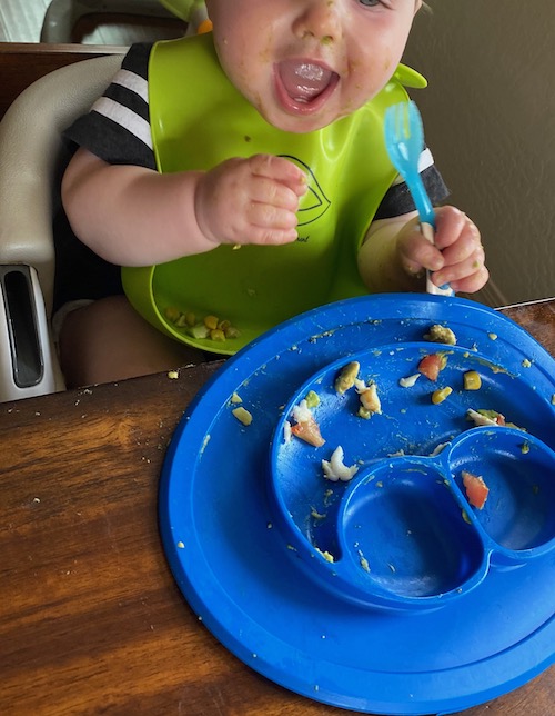 Baby boy self-feeding food at table