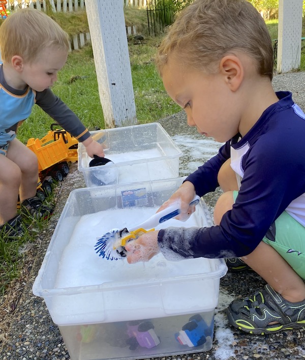 Boys playing outside with soapy water and toys in a storage bin.