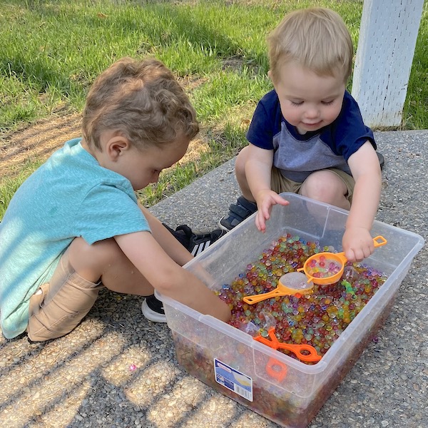 Boys playing with water beads outside in a storage bin.