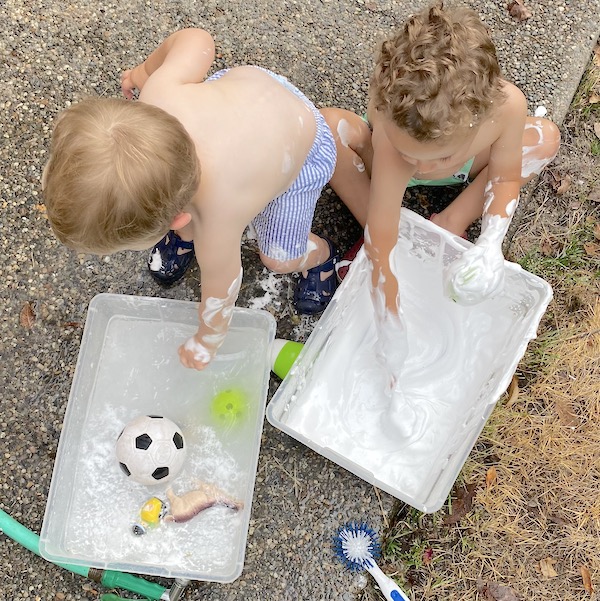 Boys playing with shaving cream in bins outside.