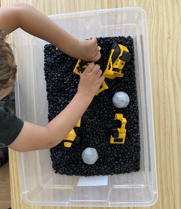 Overhead shot of boy playing with a tub of black beans and digger toys.