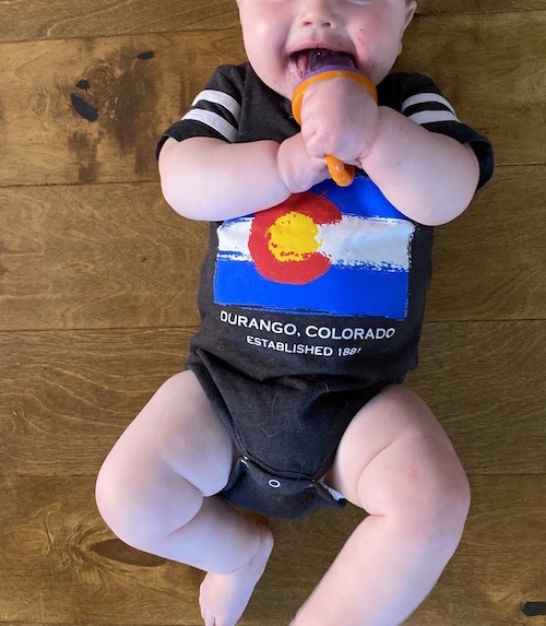 Baby laying on floor eating fruit with a silicone feeder.