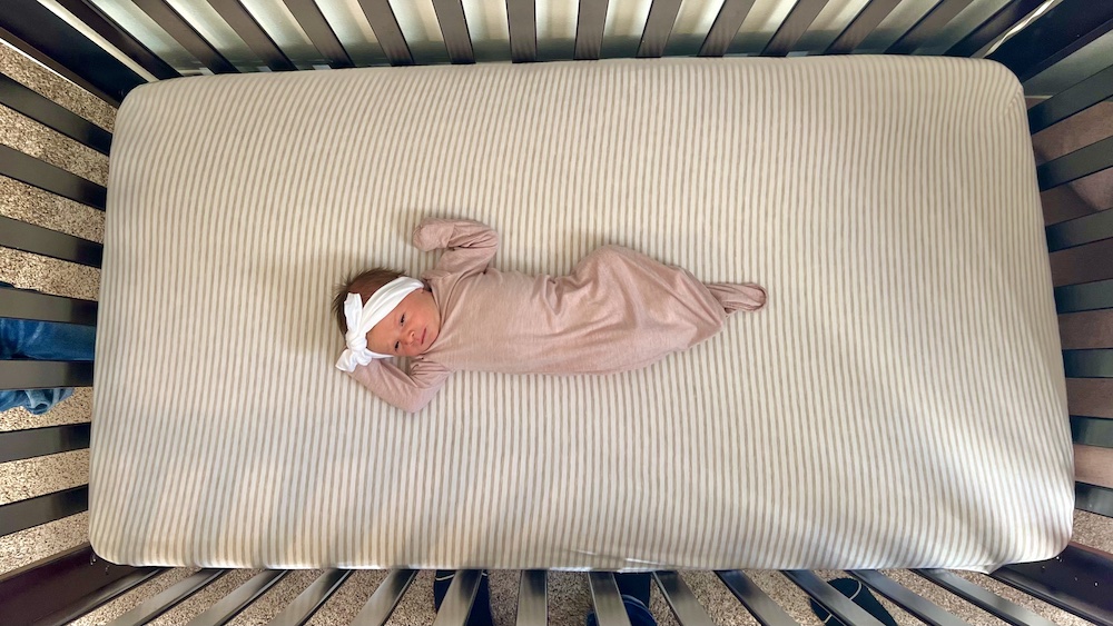 Baby in crib wearing newborn gown.