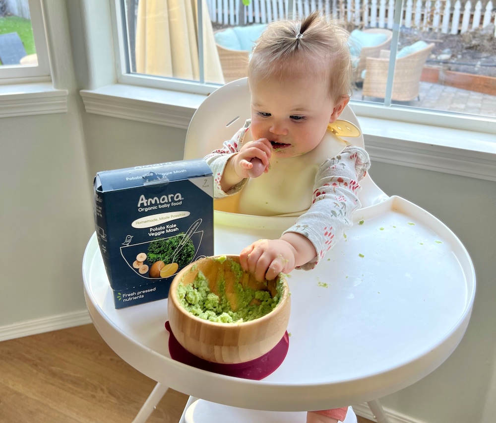 Baby with hand in bowl eating Amara baby food